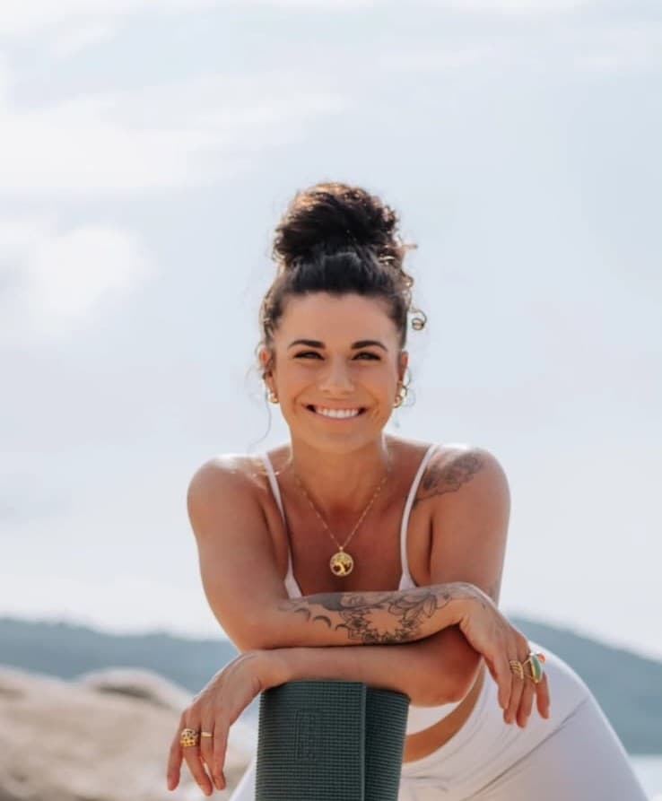 May Ternes sorrindo, apoiada em seu tapete de yoga
